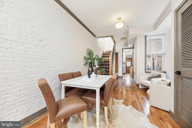 dining space with ornamental molding, brick wall, and light wood-type flooring