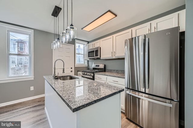 kitchen with appliances with stainless steel finishes, sink, decorative light fixtures, white cabinets, and an island with sink