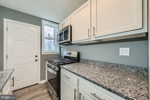 kitchen with white cabinets, light hardwood / wood-style flooring, appliances with stainless steel finishes, and dark stone counters