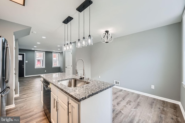 kitchen featuring sink, stainless steel appliances, hanging light fixtures, stone countertops, and a center island with sink