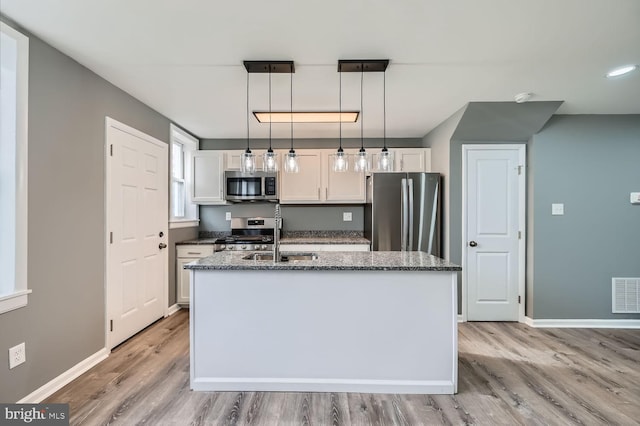 kitchen featuring white cabinets, decorative light fixtures, a kitchen island with sink, and appliances with stainless steel finishes