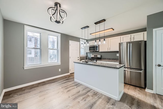 kitchen featuring white cabinetry, dark stone countertops, an island with sink, decorative light fixtures, and appliances with stainless steel finishes