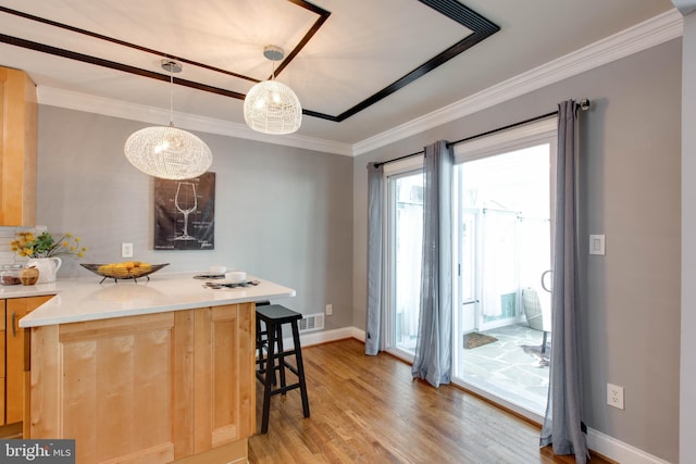 kitchen featuring pendant lighting, crown molding, a breakfast bar area, and light brown cabinetry