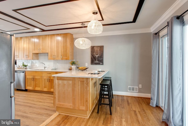 kitchen featuring a breakfast bar, light brown cabinets, appliances with stainless steel finishes, decorative light fixtures, and kitchen peninsula