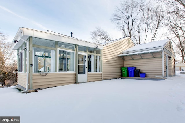 snow covered rear of property featuring a sunroom