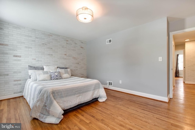 bedroom with light hardwood / wood-style flooring and brick wall