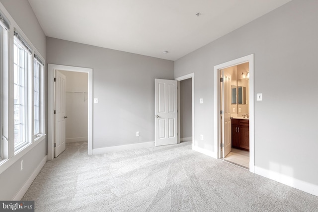 unfurnished bedroom featuring a walk in closet, a closet, light colored carpet, and connected bathroom