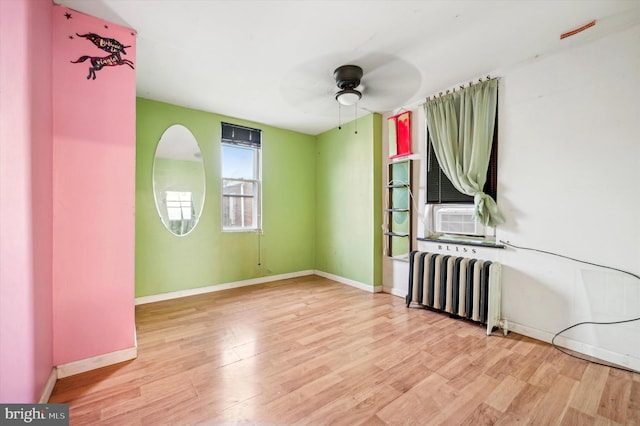 empty room featuring cooling unit, radiator heating unit, ceiling fan, and light wood-type flooring