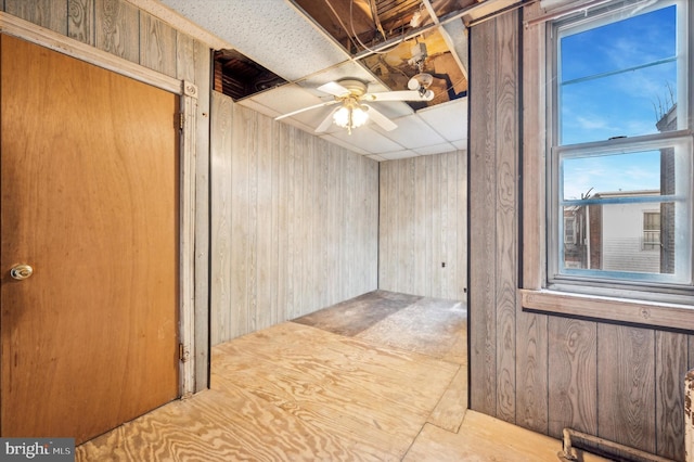 interior space with ceiling fan, wooden walls, and a paneled ceiling