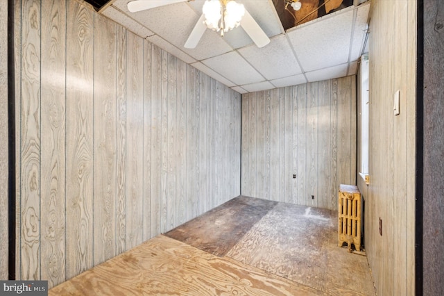 unfurnished room featuring radiator, a paneled ceiling, ceiling fan, and wood walls