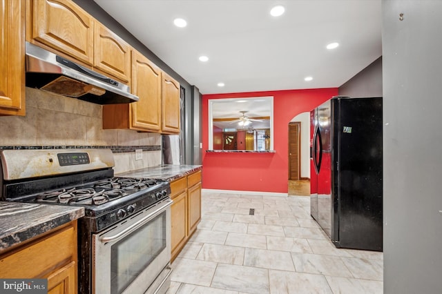 kitchen with stainless steel gas stove, black fridge, ceiling fan, dark stone counters, and decorative backsplash