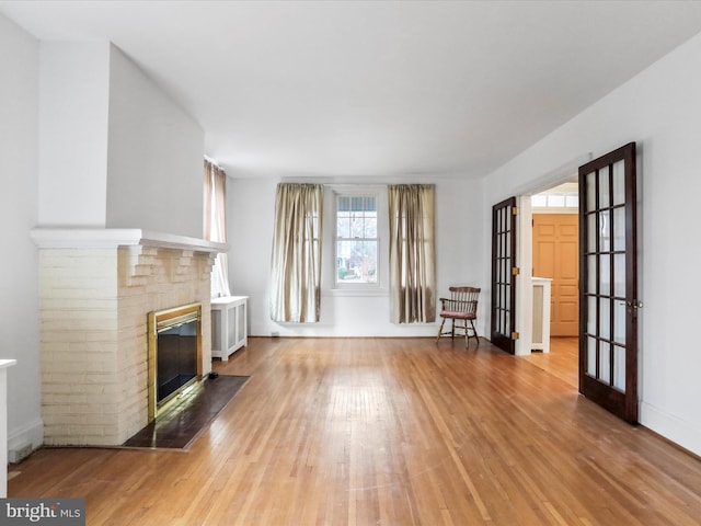 unfurnished living room featuring french doors, light hardwood / wood-style floors, and a brick fireplace