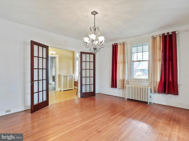 empty room featuring an inviting chandelier, wood-type flooring, radiator heating unit, and french doors