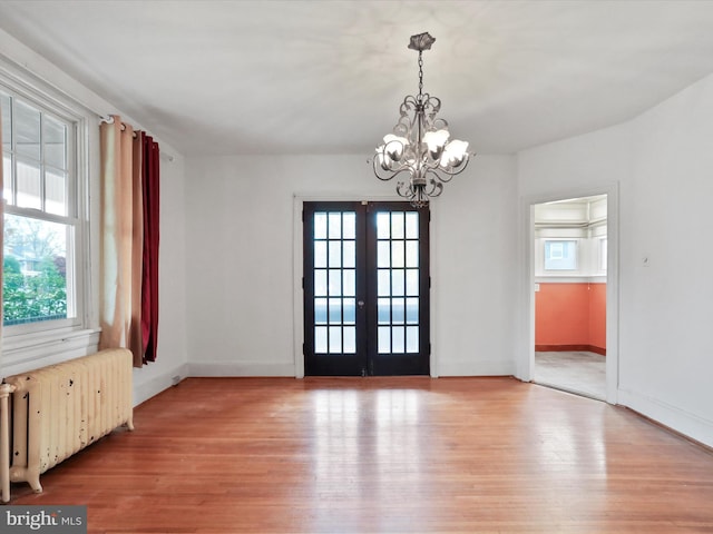 interior space featuring radiator, french doors, light hardwood / wood-style flooring, and a notable chandelier