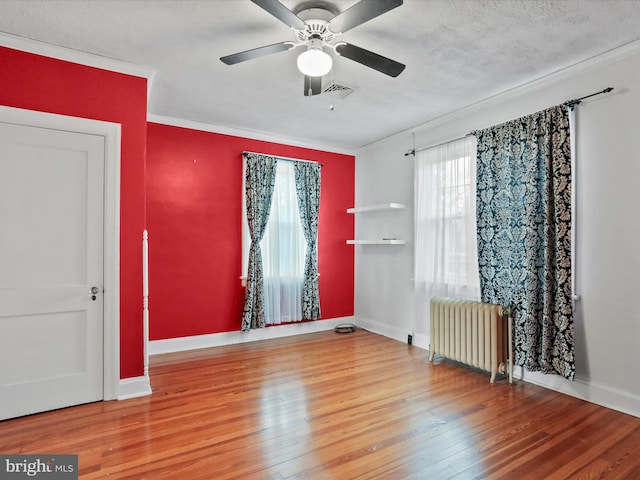 empty room with radiator heating unit, ceiling fan, ornamental molding, and wood-type flooring