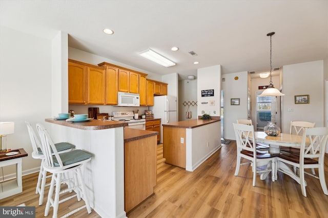 kitchen with white appliances, kitchen peninsula, decorative light fixtures, light hardwood / wood-style floors, and a kitchen bar