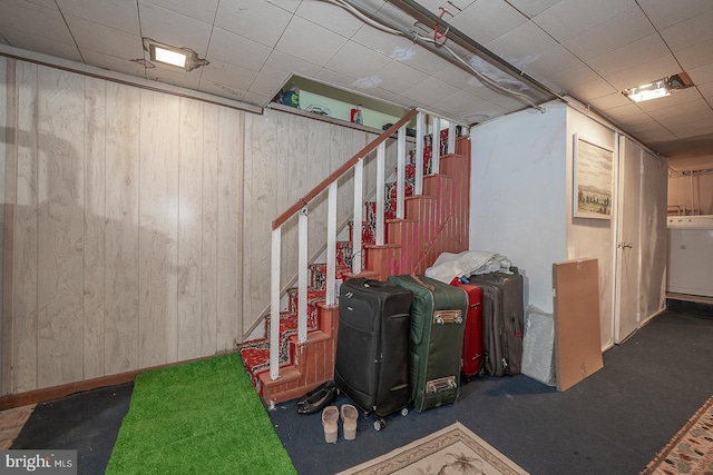 basement featuring wood walls, washer / dryer, and dark carpet