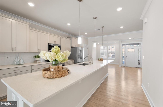 kitchen with decorative light fixtures, stainless steel refrigerator with ice dispenser, decorative backsplash, a kitchen island with sink, and sink