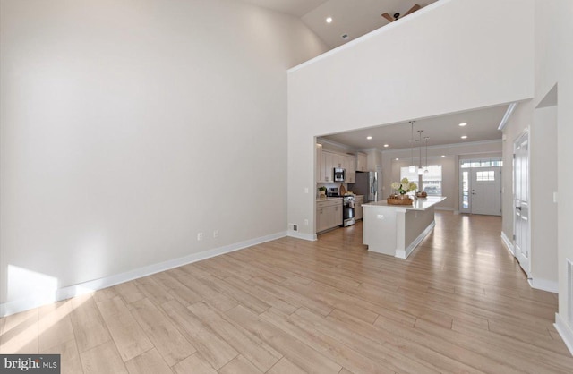 unfurnished living room featuring light hardwood / wood-style floors, ceiling fan, and high vaulted ceiling