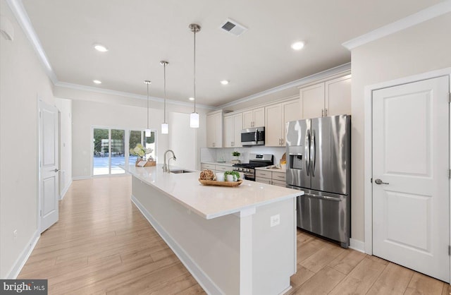 kitchen with pendant lighting, appliances with stainless steel finishes, white cabinetry, ornamental molding, and a center island with sink