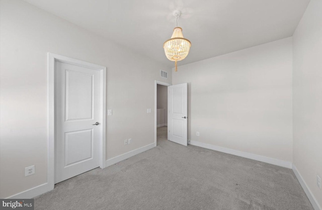 unfurnished room featuring a chandelier and light colored carpet