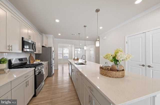 kitchen with hanging light fixtures, a kitchen island with sink, white cabinetry, appliances with stainless steel finishes, and sink