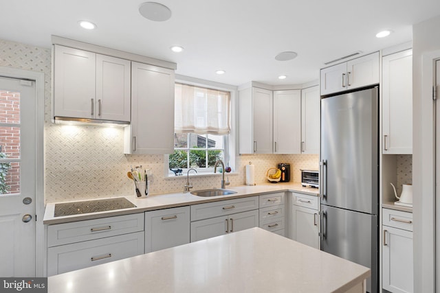 kitchen with white cabinets, sink, tasteful backsplash, stovetop, and stainless steel refrigerator