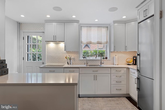 kitchen with black electric stovetop, sink, stainless steel fridge, tasteful backsplash, and white cabinetry