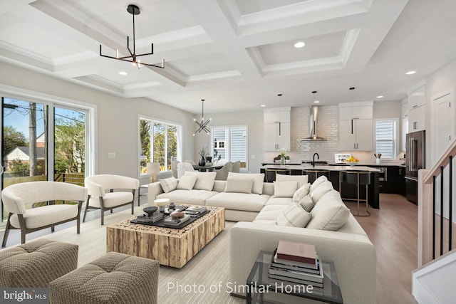 living room with plenty of natural light, light hardwood / wood-style floors, coffered ceiling, and an inviting chandelier