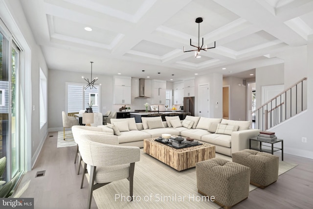 living room with light hardwood / wood-style floors, an inviting chandelier, a wealth of natural light, and coffered ceiling