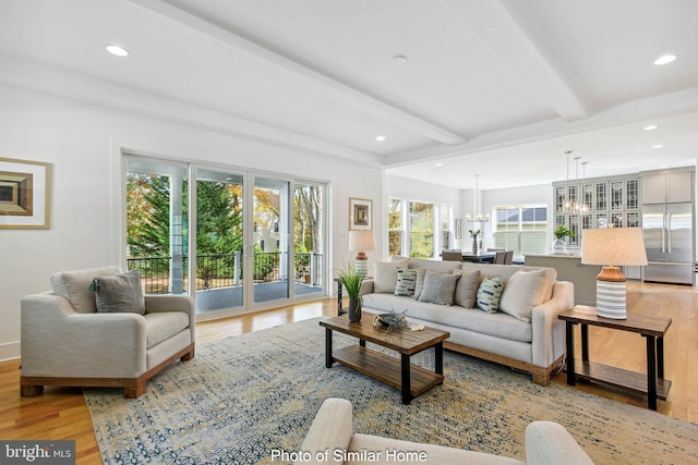 living room featuring beamed ceiling, a chandelier, and light hardwood / wood-style flooring