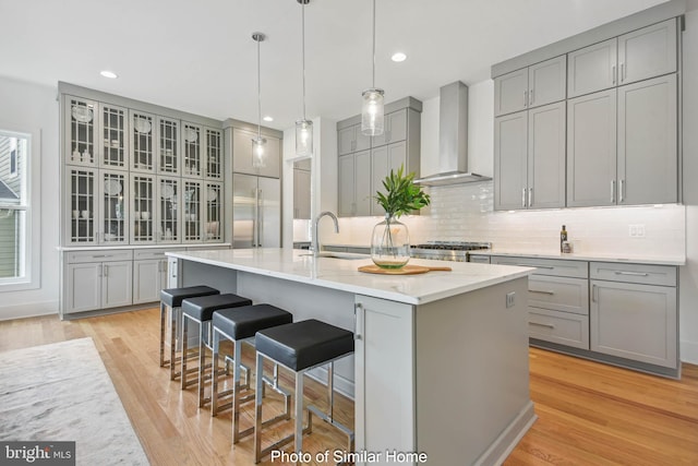 kitchen featuring wall chimney exhaust hood, gray cabinets, and an island with sink