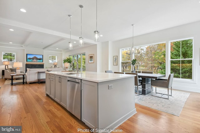 kitchen featuring light stone countertops, stainless steel dishwasher, a kitchen island with sink, sink, and gray cabinets