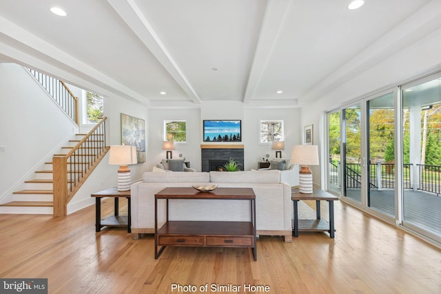 living room featuring a tile fireplace, light hardwood / wood-style flooring, and beamed ceiling