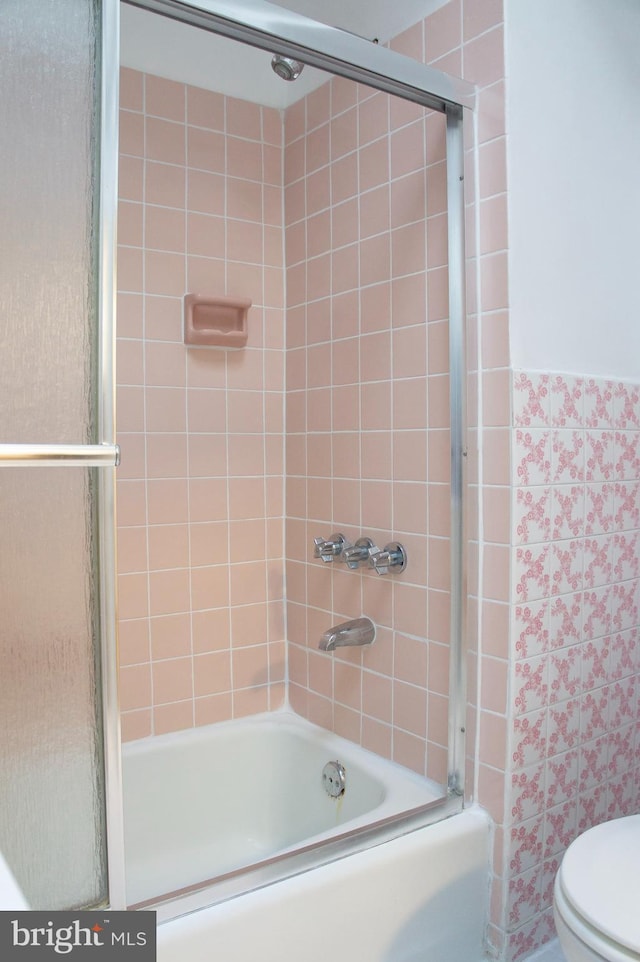 bathroom featuring shower / bath combination with glass door, toilet, and tile walls