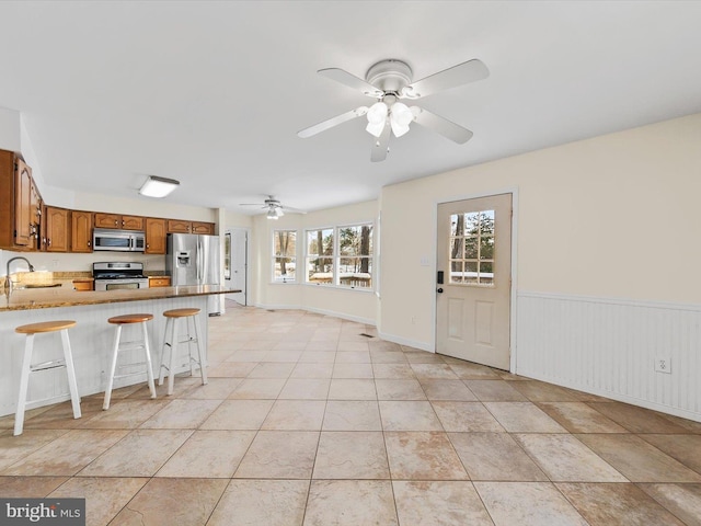 interior space with ceiling fan, a kitchen breakfast bar, kitchen peninsula, light tile patterned floors, and appliances with stainless steel finishes