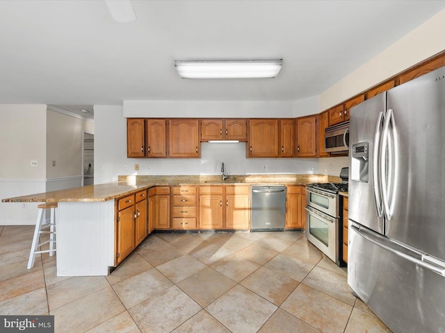 kitchen with sink, appliances with stainless steel finishes, light tile patterned flooring, light stone counters, and a breakfast bar area