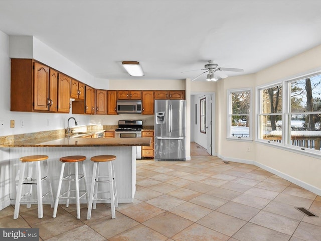 kitchen featuring ceiling fan, sink, kitchen peninsula, a kitchen bar, and appliances with stainless steel finishes