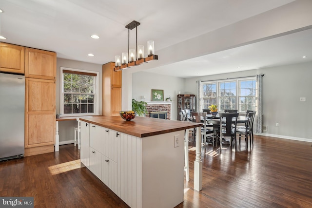 kitchen featuring dark wood-type flooring, hanging light fixtures, butcher block countertops, a kitchen island, and stainless steel refrigerator