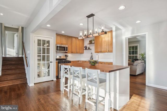 kitchen with a center island, sink, hanging light fixtures, stainless steel appliances, and butcher block countertops