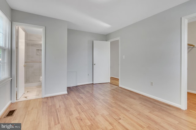 unfurnished bedroom with light wood-type flooring, a closet, a spacious closet, and ensuite bath