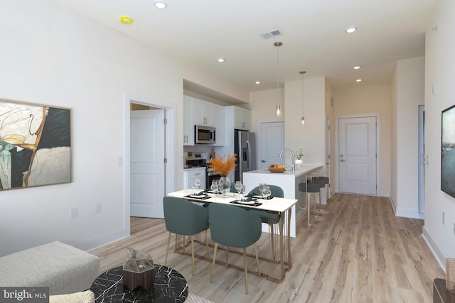 kitchen with pendant lighting, white cabinets, a kitchen breakfast bar, appliances with stainless steel finishes, and light hardwood / wood-style floors