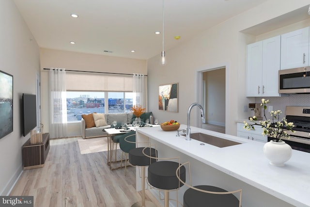 kitchen with a kitchen bar, stainless steel appliances, sink, light hardwood / wood-style flooring, and white cabinetry