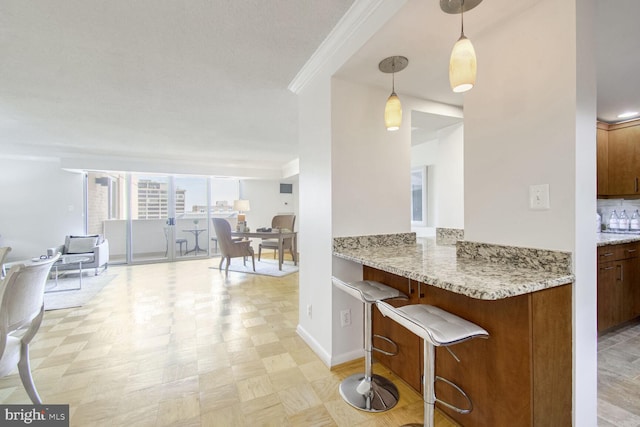 kitchen featuring a breakfast bar, crown molding, light stone counters, hanging light fixtures, and kitchen peninsula