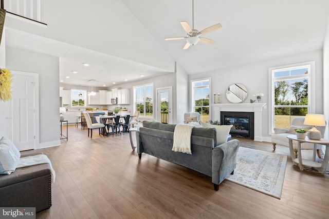 living room with ceiling fan, high vaulted ceiling, and light hardwood / wood-style flooring