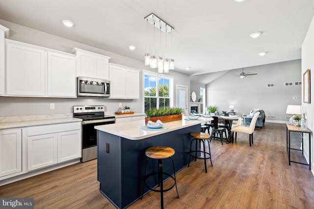 kitchen featuring stainless steel appliances, hanging light fixtures, a center island, and white cabinets