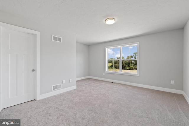 spare room with light colored carpet and a textured ceiling