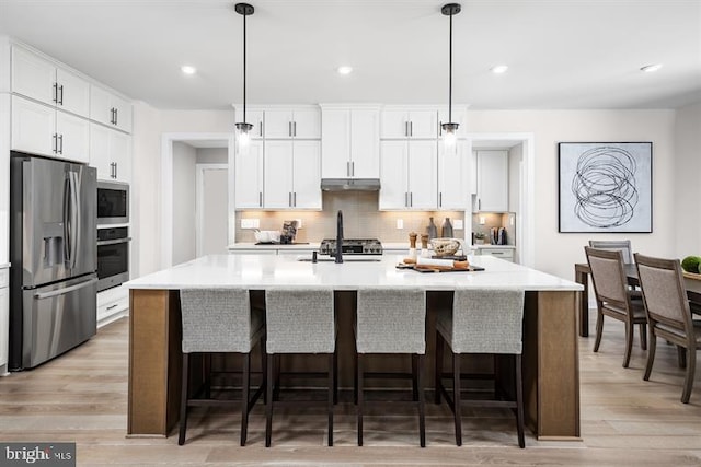 kitchen featuring pendant lighting, white cabinetry, stainless steel appliances, and a kitchen island with sink