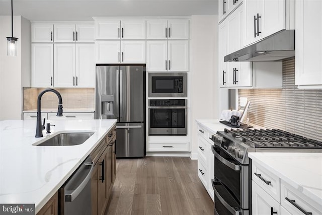 kitchen with light stone countertops, appliances with stainless steel finishes, decorative light fixtures, and sink