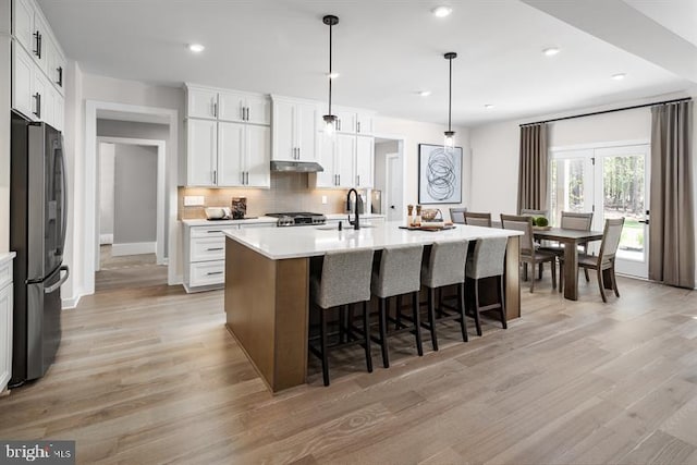 kitchen with white cabinetry, stainless steel refrigerator, and a kitchen island with sink